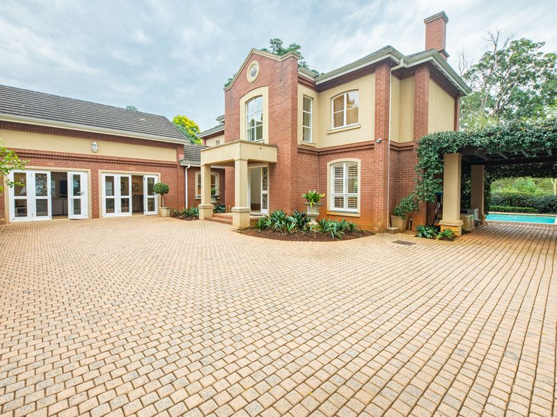 A well-maintained double-story brick residence featuring a spacious paved driveway, covered patio area, and classic architectural detailing.