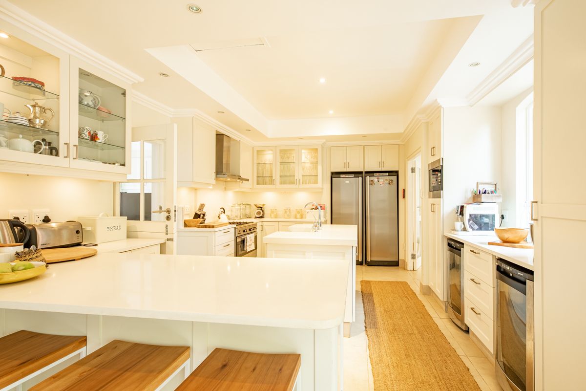 A bright, modern kitchen featuring white cabinetry, quartz countertops, a central island, and high-end integrated appliances with elegant glass-front display cabinets.