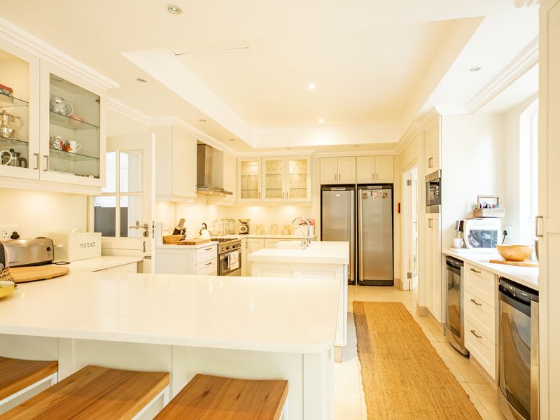 A bright, modern kitchen featuring white cabinetry, quartz countertops, a central island, and high-end integrated appliances with elegant glass-front display cabinets.