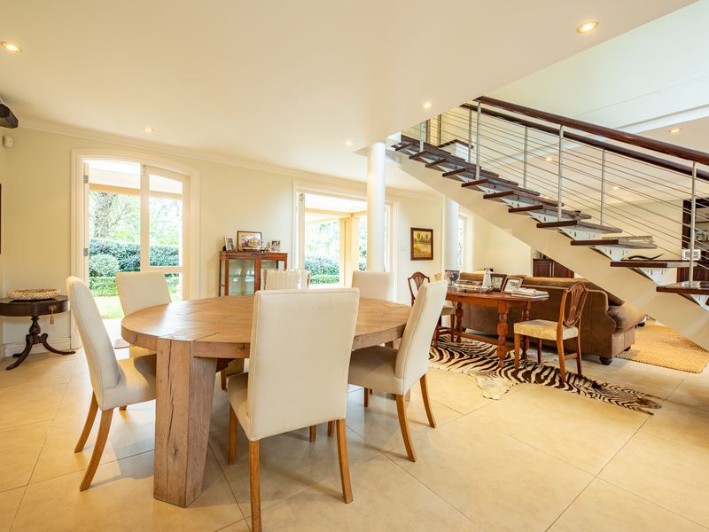 Spacious open-plan dining area featuring a modern floating staircase with stainless steel balustrades, tiled flooring, and direct access to the garden through glass doors.