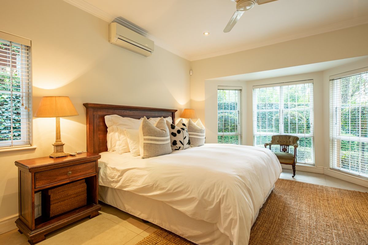 A well-lit bedroom featuring a bay window with venetian blinds, tiled flooring, a ceiling fan, and a wall-mounted split-system air conditioner.