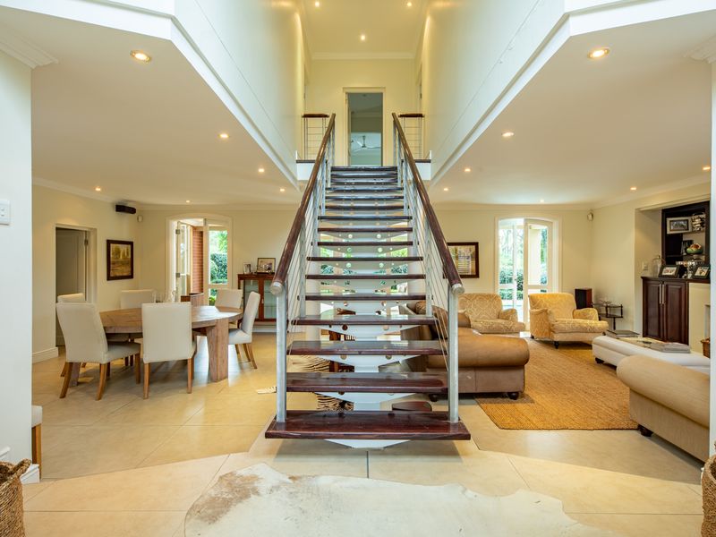 Spacious open-plan living and dining area featuring a central architectural staircase, high ceilings with recessed lighting, and large french doors leading outdoors.