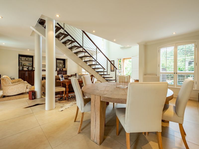 Spacious open-plan living and dining area featuring a modern staircase, tiled flooring, and large windows with plantation shutters, creating a bright and inviting atmosphere.