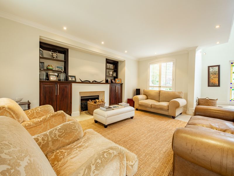 A well-maintained living room featuring built-in cabinetry, a fireplace, recessed lighting, and elegant plantation shutters, creating a warm and inviting atmosphere.