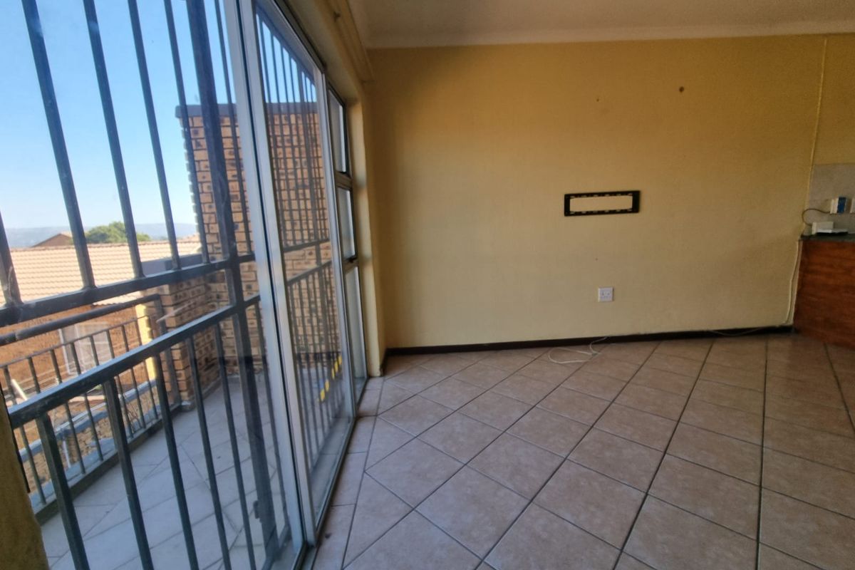 An empty living area featuring tiled flooring and a large sliding glass door with security bars, leading to an outdoor balcony space.