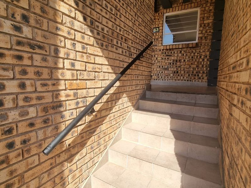 An exterior entrance staircase featuring face brick walls, tiled steps, and a black metal handrail leading to the apartment unit.