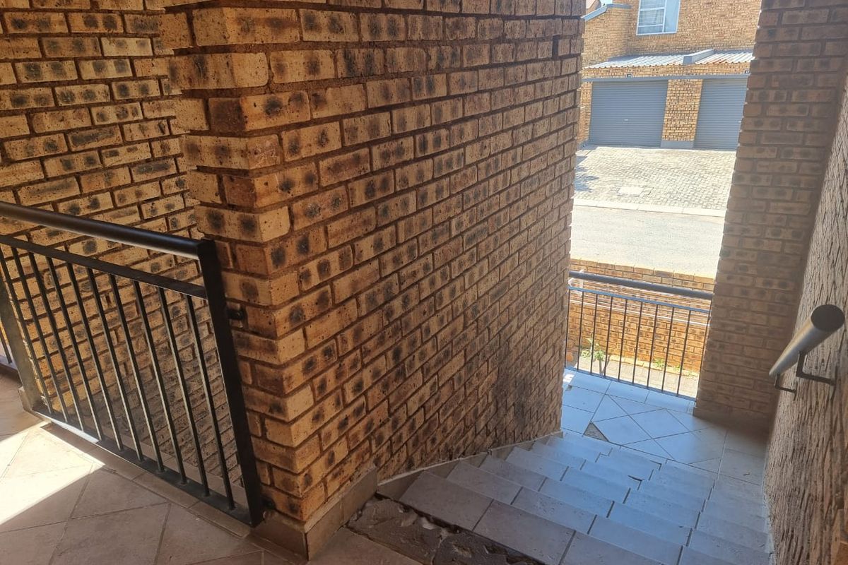 An outdoor brick staircase with metal balustrades leading to a residential complex area, showing visible wear on the tiled steps.
