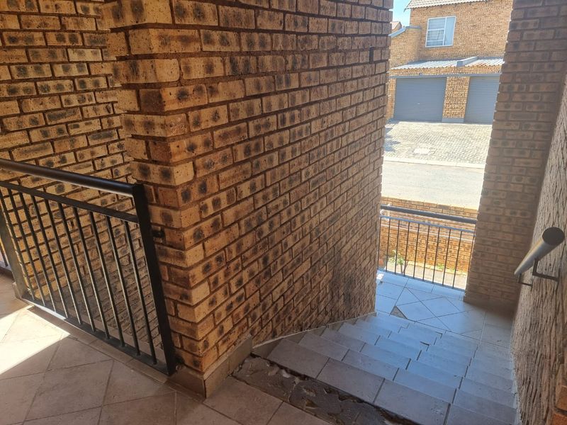 An outdoor brick staircase with metal balustrades leading to a residential complex area, showing visible wear on the tiled steps.