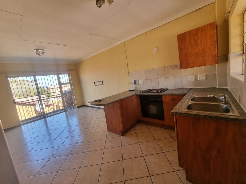 Open-plan living area featuring a functional kitchen with built-in cabinetry, oven, hob, and tiled flooring, leading to a balcony with security bars.