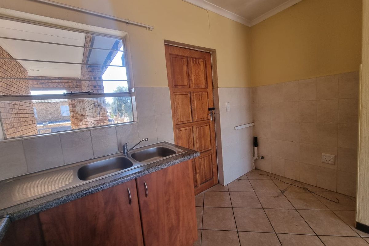 An empty kitchen area featuring wooden cabinetry, a double bowl sink, tiled splashbacks, and tiled flooring, ready for renovation or staging.