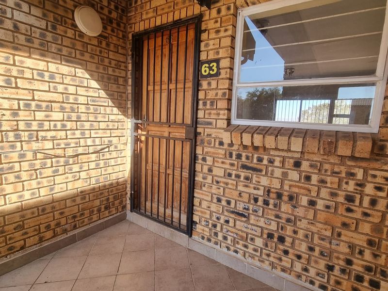 Front entrance of the apartment featuring a face brick facade, tiled porch area, and a secure metal gate.