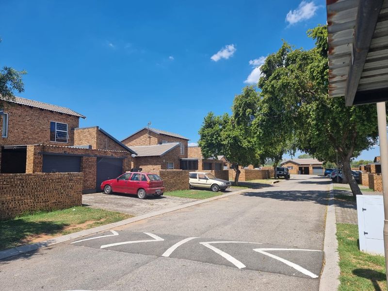 A street view of a residential apartment complex featuring face brick buildings, tiled roofs, and paved driveways with garage access.