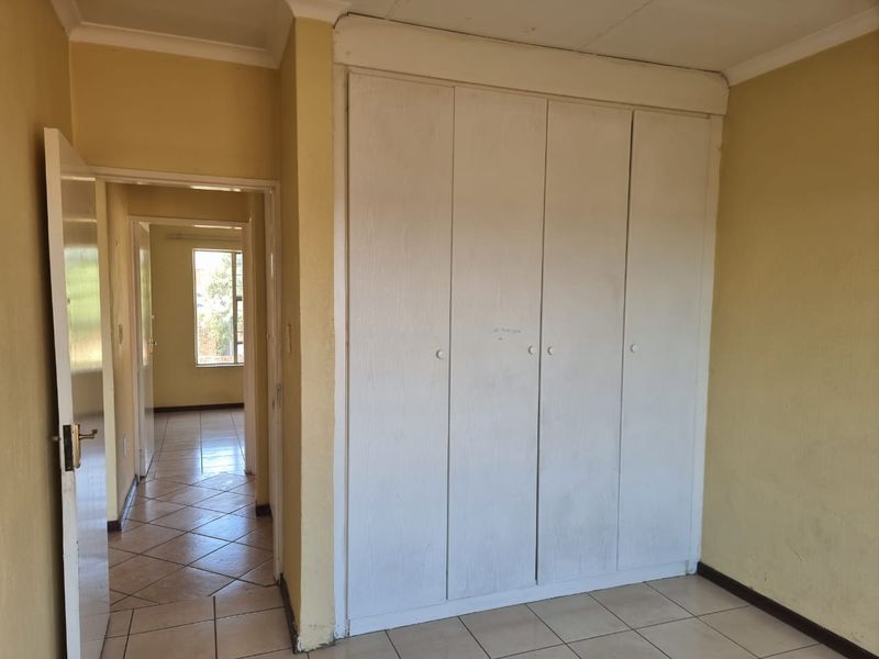 An empty bedroom featuring built-in wardrobes, tiled flooring, and neutral wall paint, with a view into the adjacent hallway.