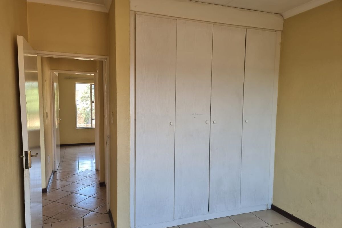 An empty bedroom featuring built-in wardrobes, tiled flooring, and neutral wall paint, with a view into the adjacent hallway.