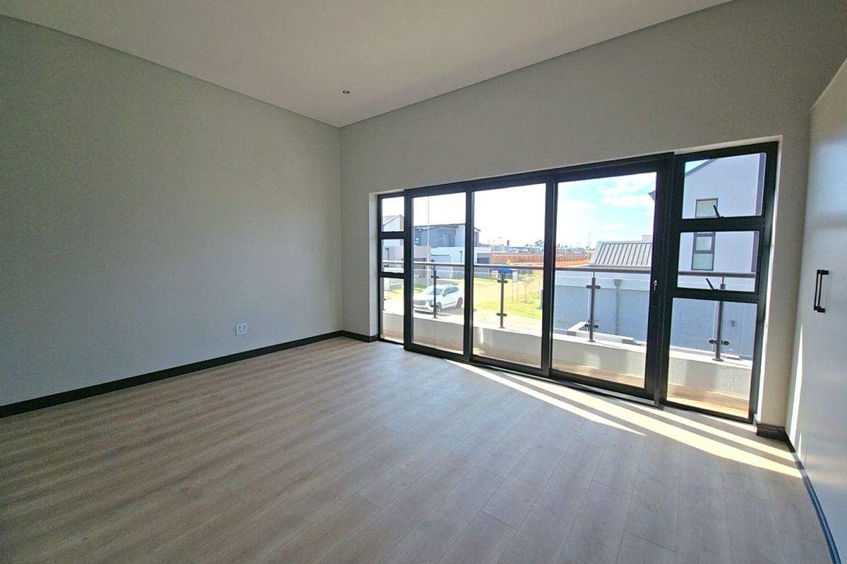 A bright, modern, and empty bedroom featuring light laminate flooring, recessed downlights, and large sliding glass doors opening onto a balcony.