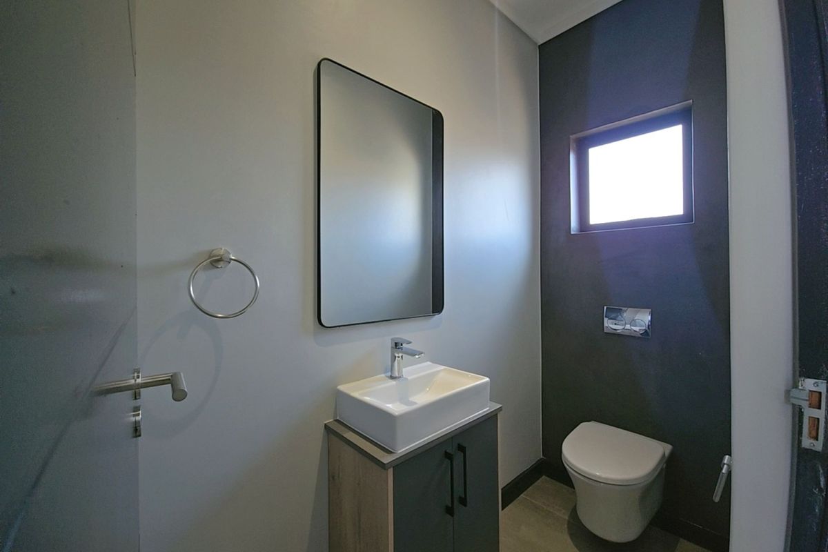 A modern, minimalist guest bathroom featuring a wall-hung toilet, a sleek vanity with a vessel sink, and a contemporary mirror.