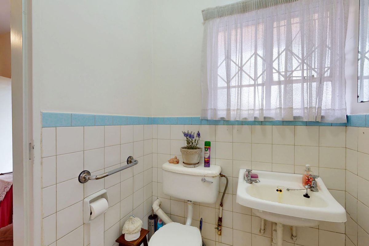 A compact bathroom featuring a standard toilet, wall-mounted washbasin, and tiled walls with a security-gated window.