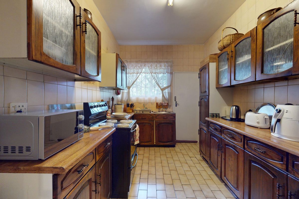 A functional galley-style kitchen featuring traditional wooden cabinetry, tiled backsplash, and tiled flooring, offering a classic aesthetic with ample storage space.