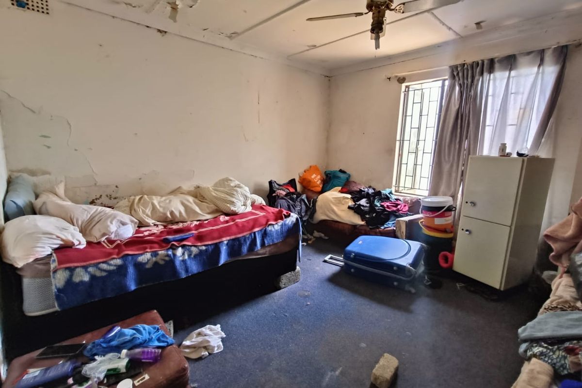 A bedroom requiring significant renovation, featuring damaged wall plaster, peeling ceiling paint, and worn carpeting.