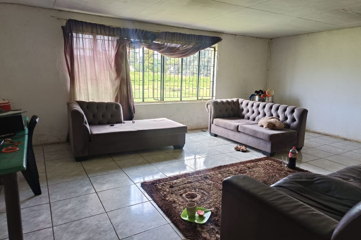 A spacious living room featuring tiled flooring, large windows with security bars, and a simple ceiling finish, offering a blank canvas for renovation.