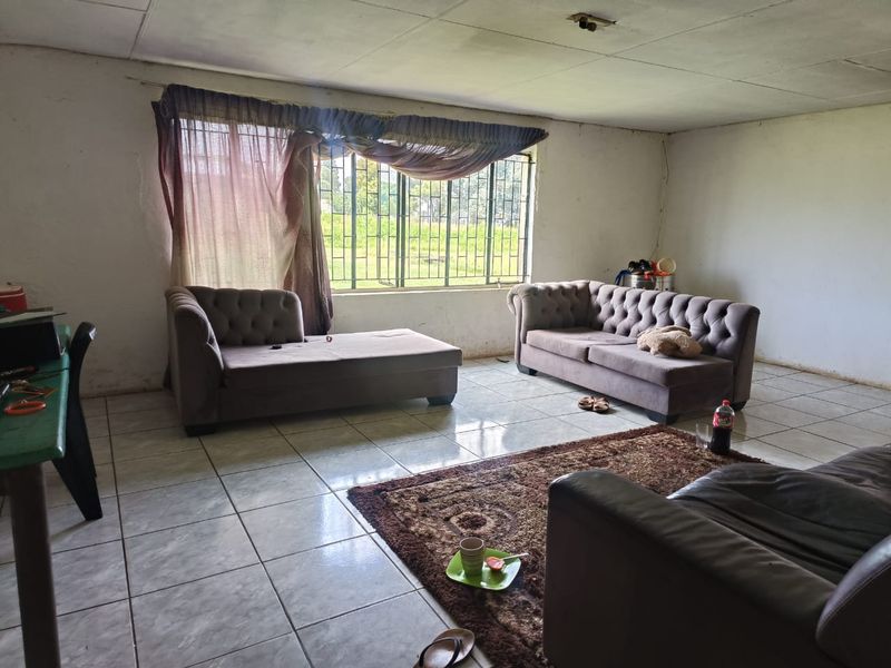 A spacious living room featuring tiled flooring, large windows with security bars, and a simple ceiling finish, offering a blank canvas for renovation.