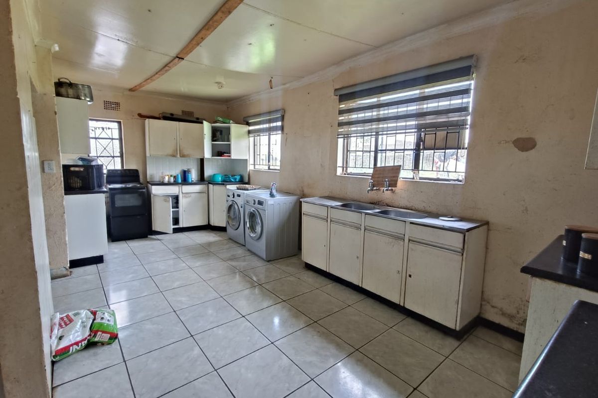 A functional kitchen and laundry area featuring tiled flooring, built-in cabinetry, double sink, and space for laundry appliances.