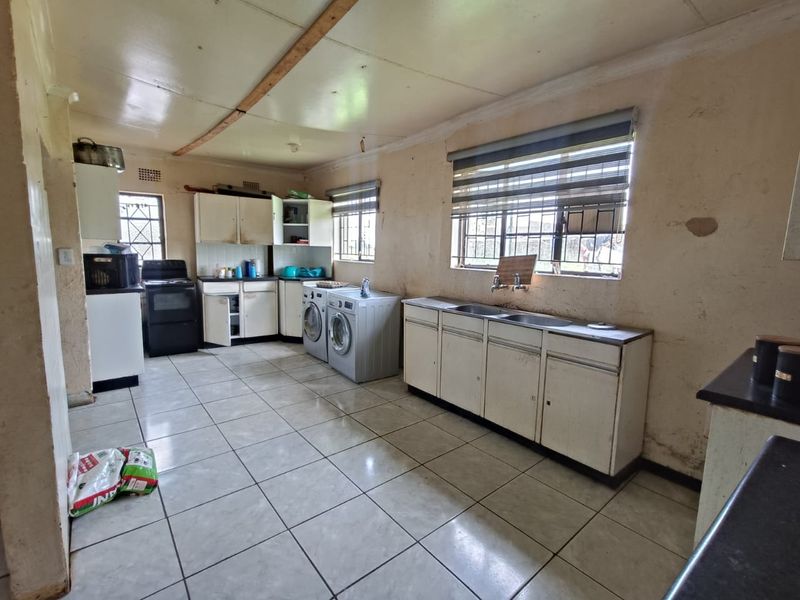A functional kitchen and laundry area featuring tiled flooring, built-in cabinetry, double sink, and space for laundry appliances.