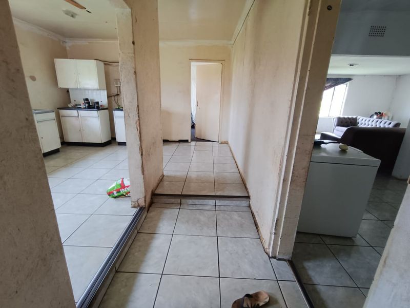 A view from a hallway looking into a kitchen and adjacent living area, featuring tiled flooring and dated interior finishes throughout.