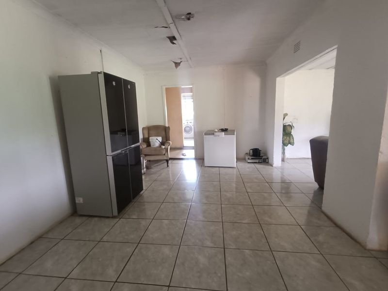 Open plan living area featuring tiled flooring and direct access to adjacent utility space, requiring cosmetic updates and ceiling repairs.
