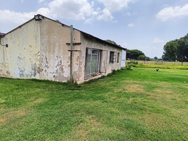 Exterior view of a farm building showing significant wear to the exterior plaster and paint, set within a large open grass field.