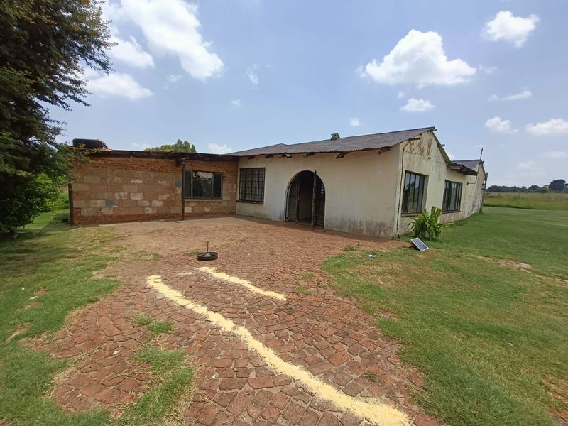 Exterior view of a farm dwelling featuring a brick and plaster facade, arched entrance, and a paved courtyard area requiring maintenance and restoration.