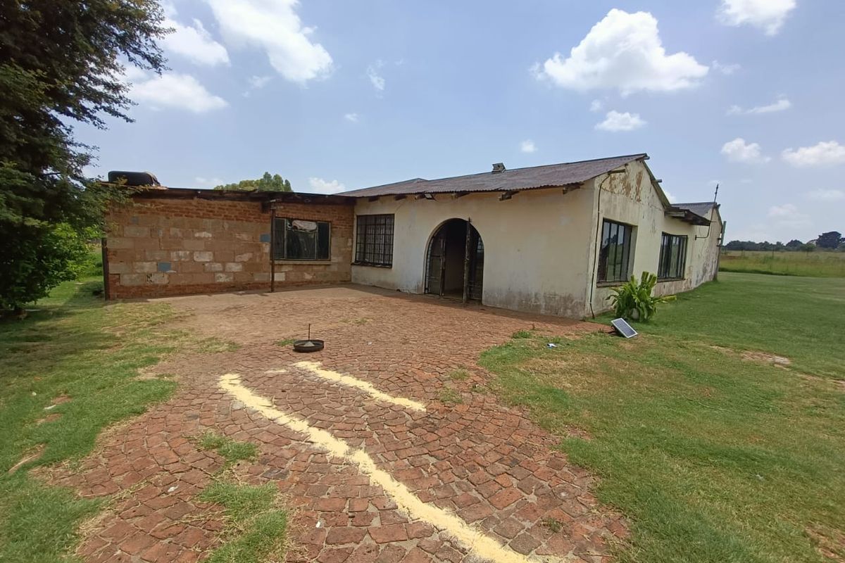 Exterior view of a farm dwelling featuring a brick and plaster facade, arched entrance, and a paved courtyard area requiring maintenance and restoration.