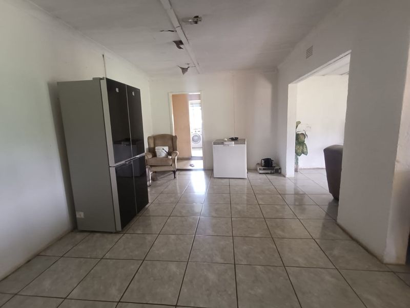 An open-plan living area featuring tiled flooring and a damaged ceiling, providing a blank canvas for renovation.