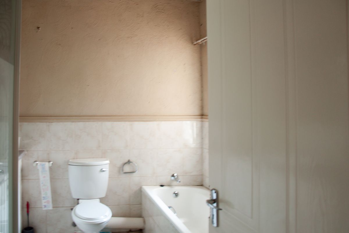 A dated bathroom featuring a standard bathtub, toilet, and tiled splashbacks, requiring cosmetic updates to modernize the space.