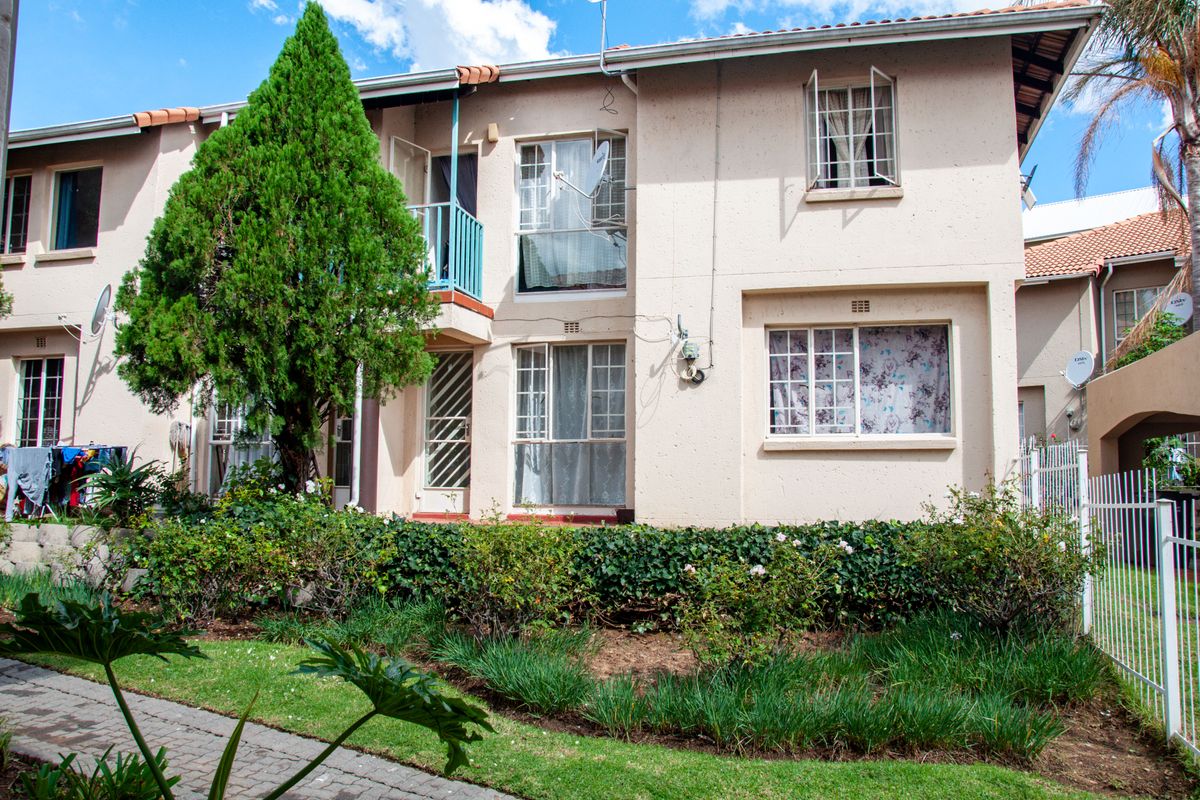 Exterior view of a multi-story apartment building featuring a paved walkway, landscaped garden, and balcony access.