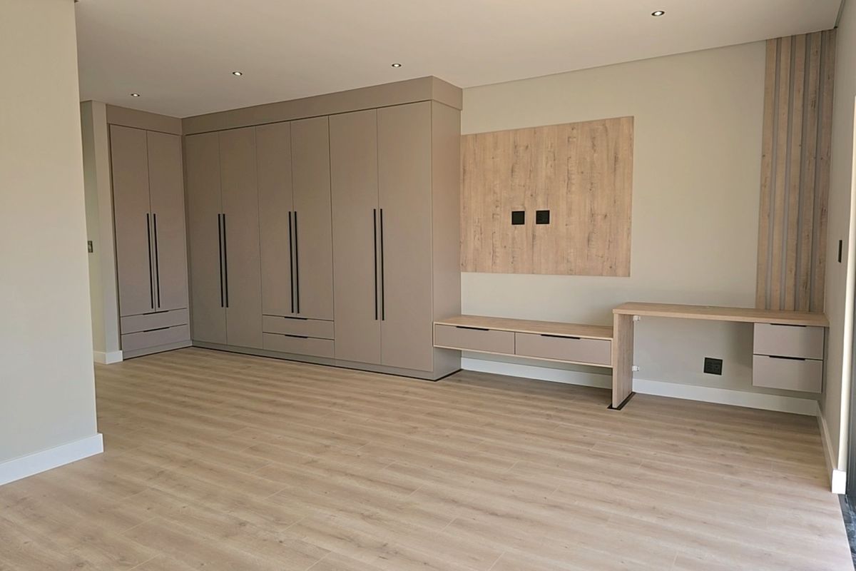Spacious bedroom featuring modern built-in cupboards, a sleek integrated desk, floating media console, and high-quality laminate flooring with recessed lighting.