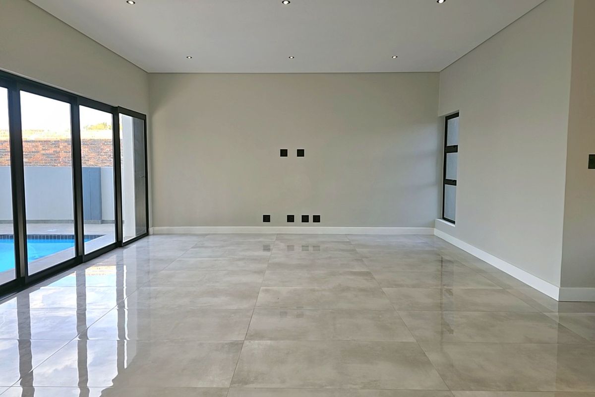 Spacious, modern living area featuring large format porcelain tiles, recessed downlighting, and expansive sliding doors providing direct access to the pool area.