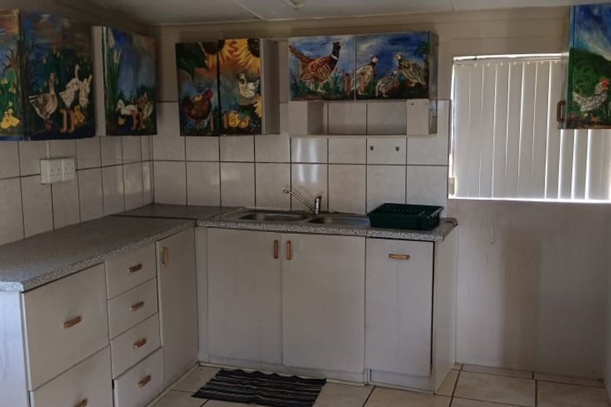 A functional kitchen area featuring tiled splashbacks, double sink, and custom-painted cabinetry, offering a practical workspace with natural light from vertical blinds.