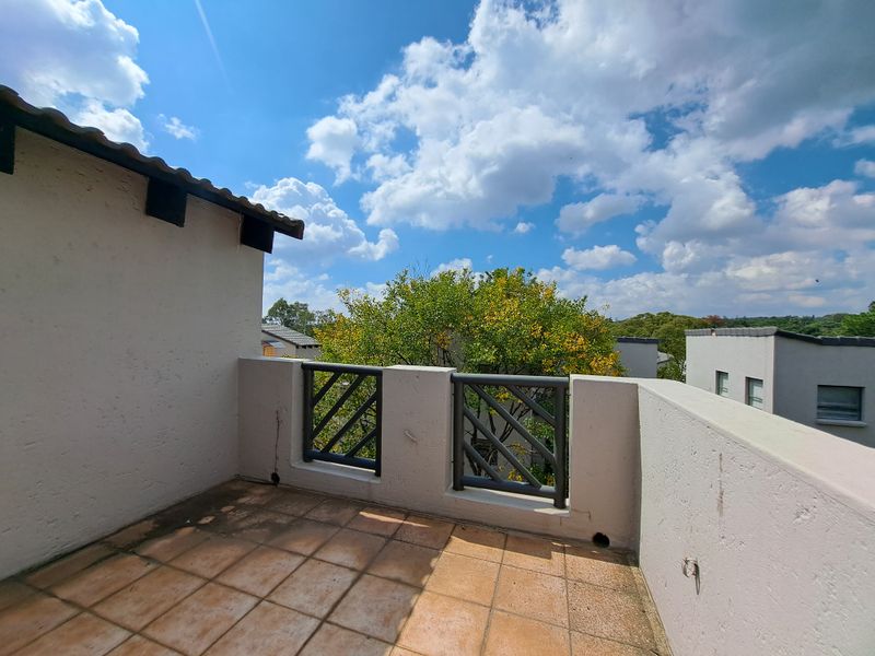 An open-air balcony featuring tiled flooring and a metal balustrade, offering an elevated outdoor space with views of the surrounding neighborhood.