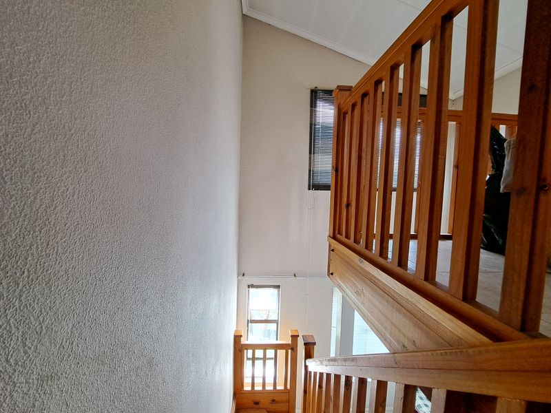A view of an interior staircase featuring wooden railings and a high vaulted ceiling, connecting different levels of the apartment.