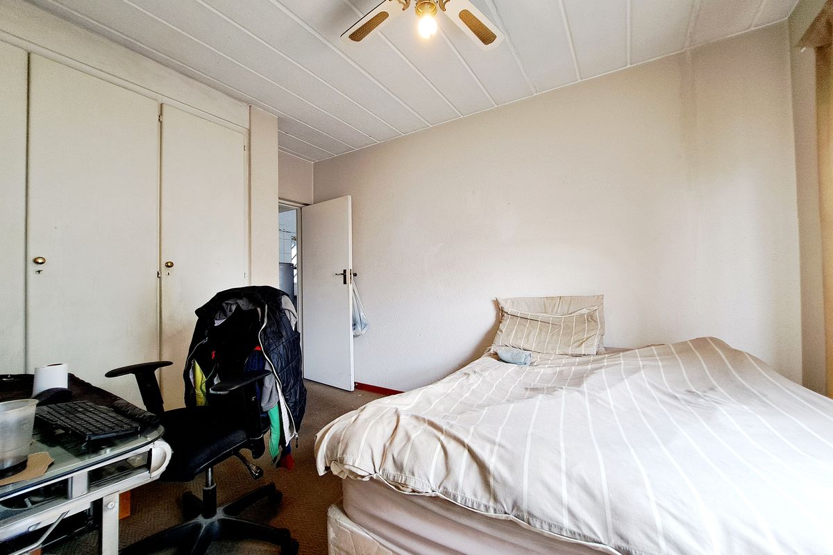 A bedroom featuring built-in cupboards, a ceiling fan, and carpeted flooring. The room shows signs of wear and requires cosmetic updates.