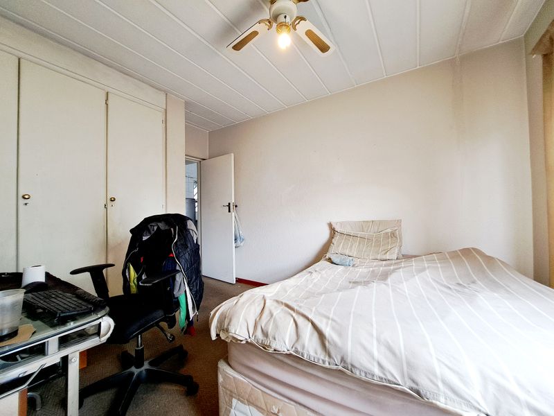 A bedroom featuring built-in cupboards, a ceiling fan, and carpeted flooring. The room shows signs of wear and requires cosmetic updates.
