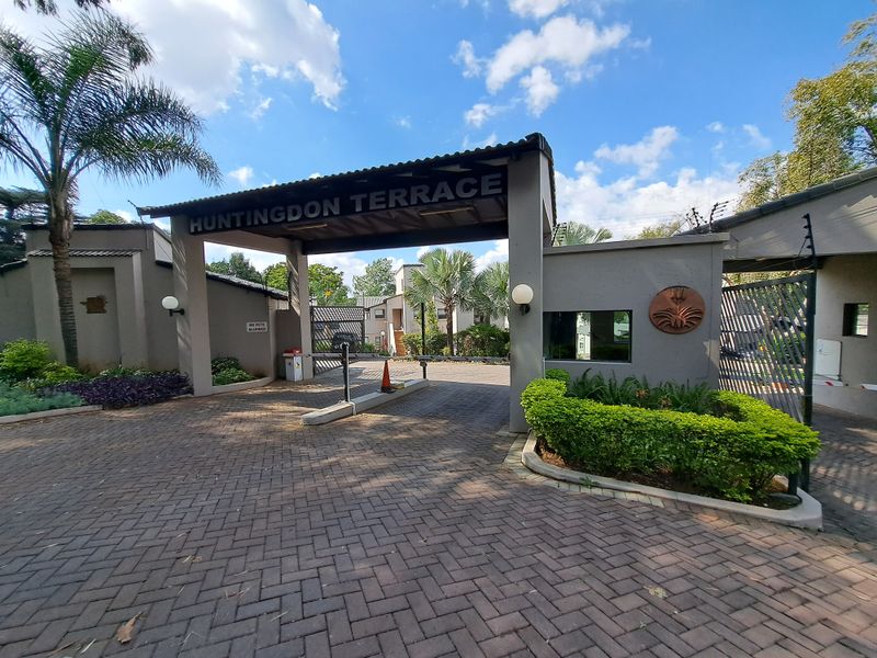The main entrance to Huntingdon Terrace apartment complex, featuring a secure gated access point with paved driveway and established landscaping.
