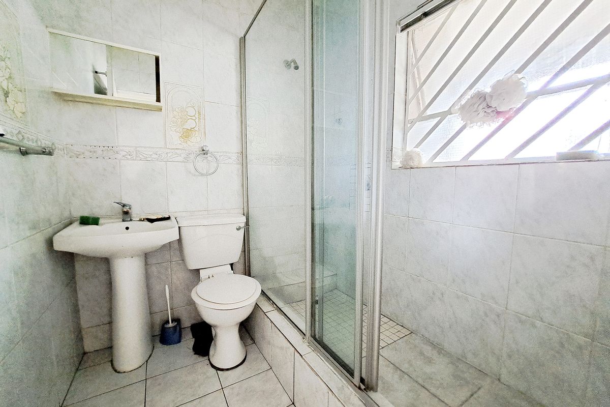 A functional bathroom featuring a pedestal basin, toilet, and a glass-enclosed shower with tiled finishes throughout.
