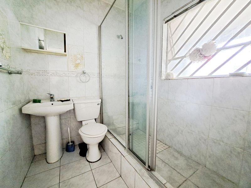 A functional bathroom featuring a pedestal basin, toilet, and a glass-enclosed shower with tiled finishes throughout.