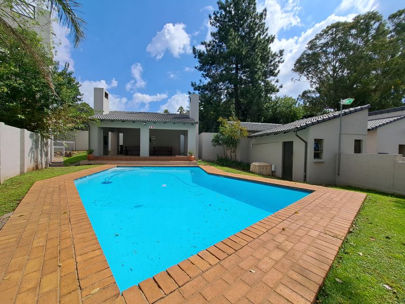 Outdoor pool area featuring a swimming pool with brick coping, adjacent lawn, and a covered patio structure with a tiled roof.