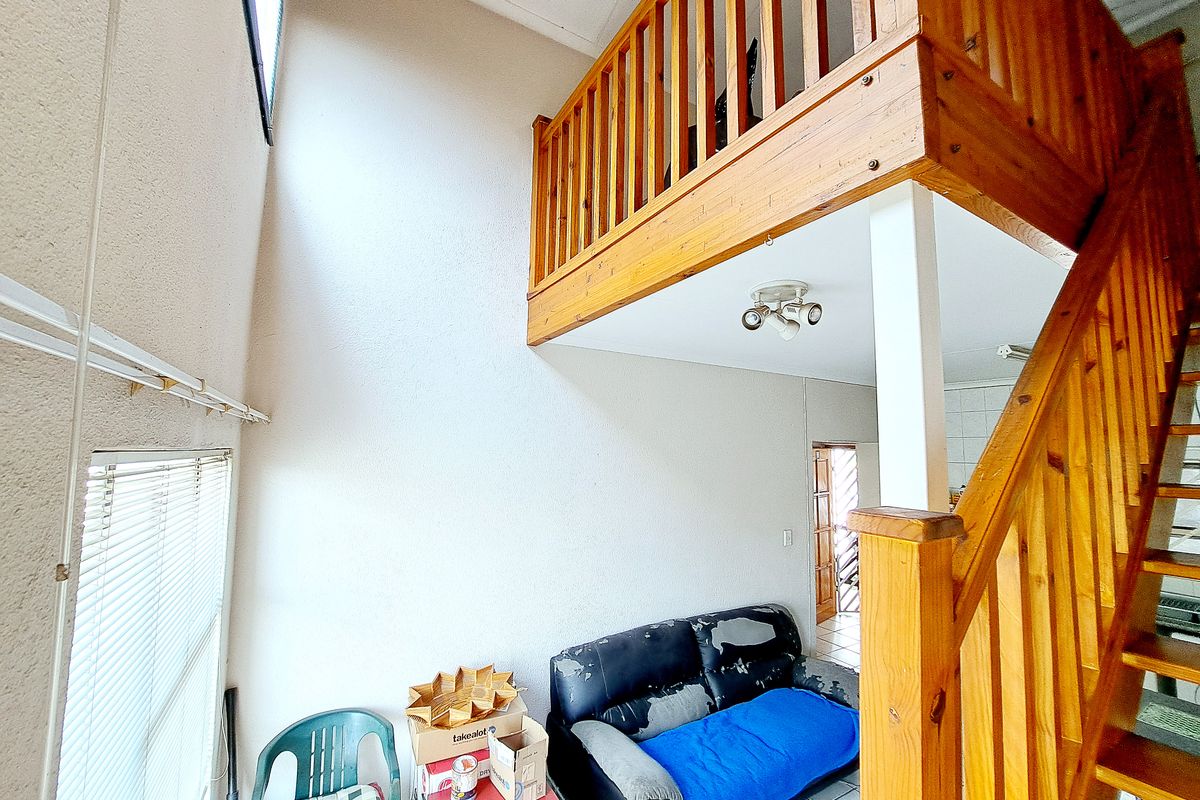 Living area featuring a wooden staircase leading to a mezzanine level with timber balustrades and tiled flooring throughout.