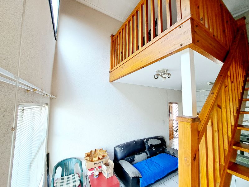 Living area featuring a wooden staircase leading to a mezzanine level with timber balustrades and tiled flooring throughout.