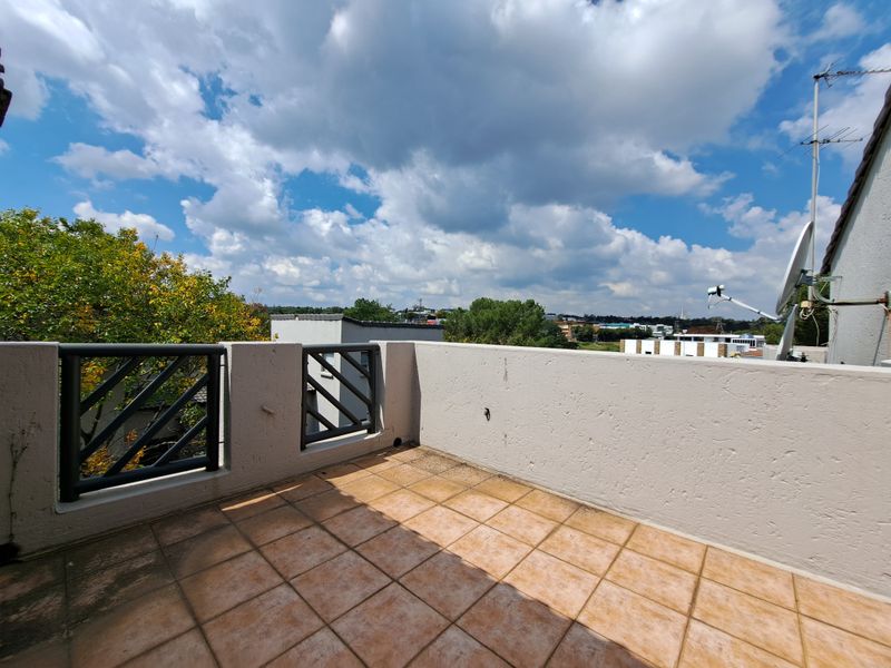 An open-air balcony featuring tiled flooring and a metal balustrade, offering elevated views of the surrounding neighborhood.