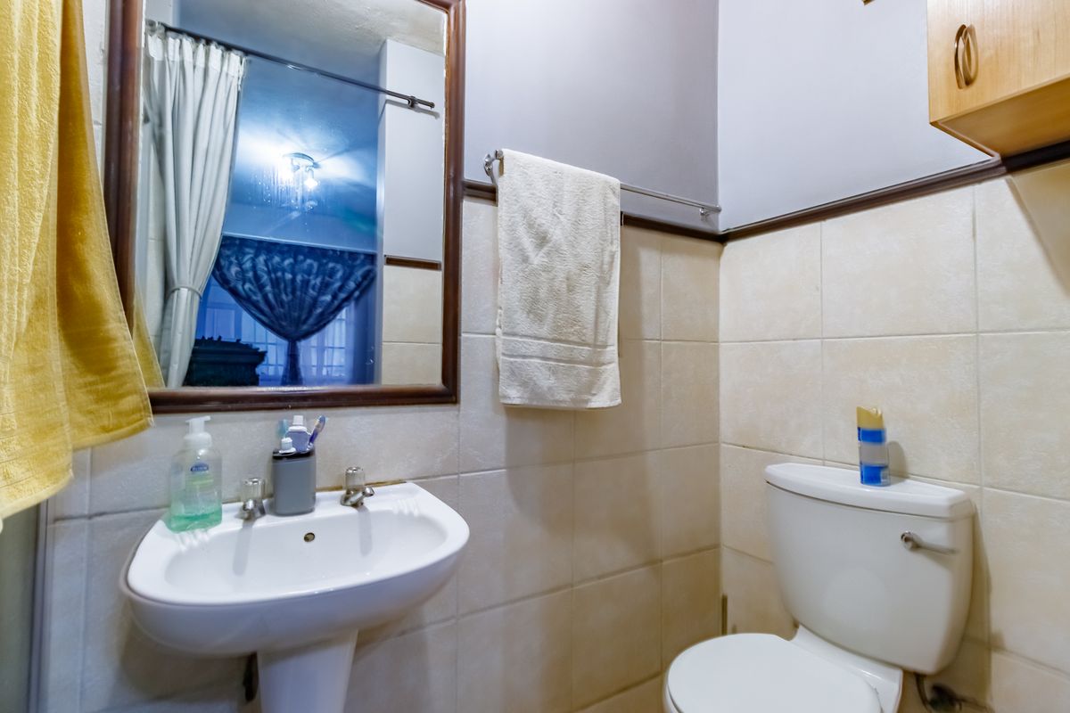 A functional bathroom featuring a pedestal washbasin, toilet, wall-mounted mirror, and tiled wall finishes.